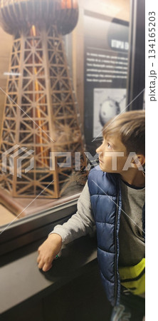 A young boy looks at an information panel and a large model of a structure behind glass at an exhibition and presses a button. The concept is a children's museum experience and scientific research. 134165203