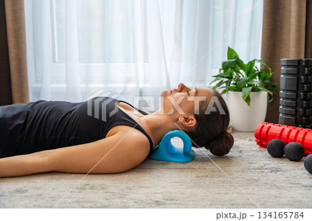 Young woman lies on the floor using a blue cervical traction device to stretch the neck. Home therapy for neck pain, muscle tension and spine decompression. 134165784