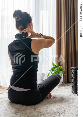 Young woman sitting on the floor at home using a massage ball to relieve neck pain. Self care routine for muscle tension and cervical spine health. Young woman sitting on the floor at home using a massage ball to relieve neck pain. Self care routine for muscle tension and cervical spine health. 134165803