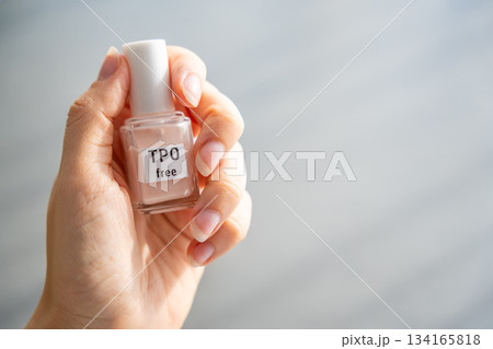 Woman holding a bottle of TPO free gel polish in bright natural light. Safe manicure product without Trimethylbenzoyl Diphenylphosphine Oxide for health-conscious consumers. 134165818