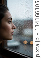 雨に濡れた窓の外を見つめる女性 134166305