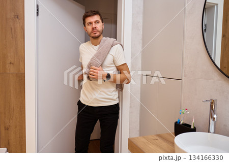 Man standing in bathroom holding towel on shoulder and opening door after hygiene routine 134166330