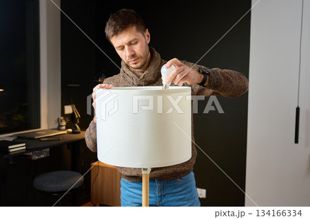 Man replacing light bulb in floor lamp while standing in home interior Man replacing light bulb in floor lamp while standing in home interior 134166334