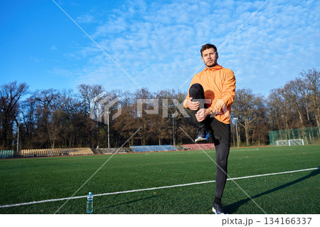 Man stretching leg while standing on sports field at outdoor stadium 134166337