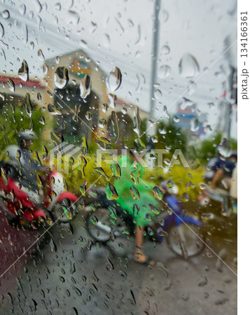 View of active Thai motorcycle and bike traffic through glass with raindrops, people in raincoats, focus on raindrops View of active Thai motorcycle and bike traffic through glass with raindrops, people in raincoats, focus on raindrops 134166361