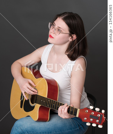 Confident female guitarist with chill expression on face, happily strumming away on classical six string acoustic guitar, totally focused on music during practice session. Guitar player from zoomers 134166365