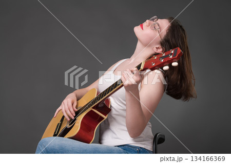 Woman guitarist performs piece of music with passion and talent, impressively using acoustic guitar. Musician wearing glasses with her eyes closed. Woman playing guitar with incredible skill, passion 134166369