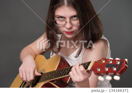 Woman guitarist rock musician performing piece of music on classical six steel string acoustic guitar. Young adult musician wearing glasses looking camera. Woman guitar player plucking spanish guitar Woman guitarist rock musician performing piece of music on classical six steel string acoustic guitar. Young adult musician wearing glasses looking camera. Woman guitar player plucking spanish guitar 134166371