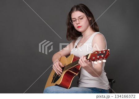 Female guitarist performing piece of music on classical guitar. Musician wearing glasses focusing intently on strings. Young adult European woman musician plays six string guitar. She member of Gen Z 134166372