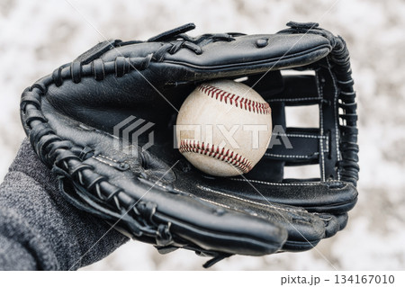 Close up of hand holding black leather baseball glove with white baseball inside, outdoor sports equipment, focus on texture and detail, energetic mood 134167010