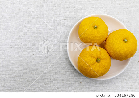 冬至の準備:白い皿に盛られた柚子三つと布地の背景 冬至の準備:白い皿に盛られた柚子三つと布地の背景 134167286