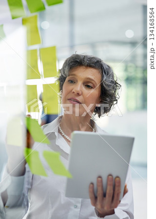 Glass wall, tablet and business woman writing, planning and strategy in office workplace. Sticky notes, brainstorming and senior female professional with technology for working, schedule and info. Glass wall, tablet and business woman writing, planning and strategy in office workplace. Sticky notes, brainstorming and senior female professional with technology for working, schedule and info. 134168564