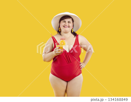 Fat woman in red swimsuit and beach hat holding cocktail isolated on yellow background. 134168849