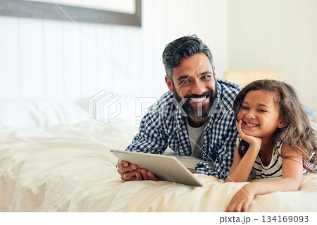 Happy, portrait and digital tablet by girl with father on a bed, relax and browsing for entertainment in their home. Face, smile and parent and with child in bedroom online for streaming or reading Happy, portrait and digital tablet by girl with father on a bed, relax and browsing for entertainment in their home. Face, smile and parent and with child in bedroom online for streaming or reading 134169093