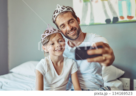 Man, girl child and selfie in princess tiara, happiness with love and care at family home. Smile in picture, father and daughter bonding with crown, happy people spending time together in bedroom 134169523