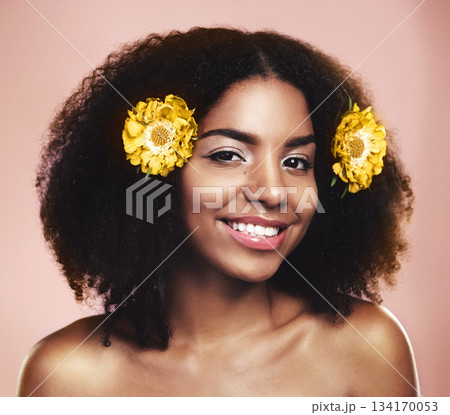Portrait of happy woman, hair care and face with yellow flowers, natural beauty or pink background in studio. African model, skincare and daisy plants in afro for sustainable cosmetics, smile or glow 134170053