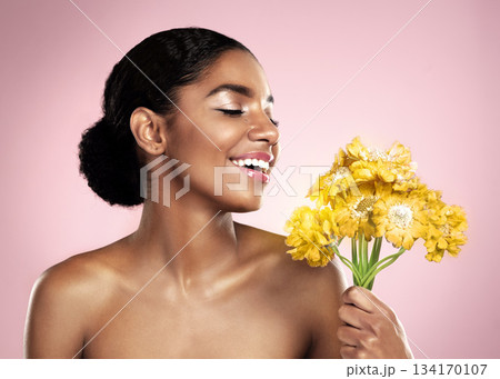 Happy woman, yellow flowers and natural skincare in studio, pink background and eco friendly makeup cosmetics. African model, beauty and smile with daisy plants, happiness and glow of floral facial 134170107