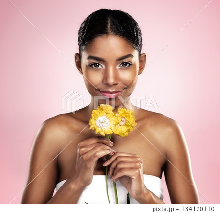 Portrait, woman and flowers for skincare in studio, pink background and eco friendly cosmetics. Face, african model and natural beauty with yellow daisy, plants and sustainability for floral blossom 134170110