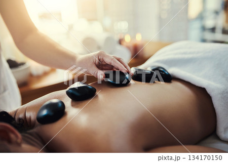 Woman, hands and rocks for back massage at spa in beauty relaxation or skincare on bed. Hand of masseuse applying hot rock or stones on female for physical therapy, zen or skin treatment at resort 134170150