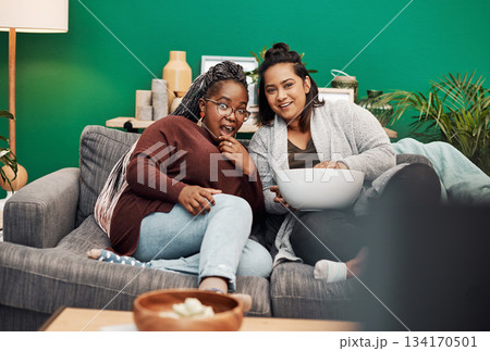 Girl friends, tv and surprise in home living room on a couch with a happy smile. Series, movie and women together in a lounge with a female friend looking at a television in house with popcorn 134170501