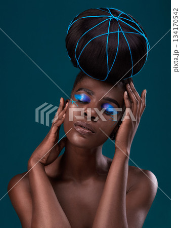 Face, hair and makeup with a model black woman in studio on a blue background for beauty. Hands, haircare and cosmetics with an attractive young female person at the salon for fashion or styling Face, hair and makeup with a model black woman in studio on a blue background for beauty. Hands, haircare and cosmetics with an attractive young female person at the salon for fashion or styling 134170542