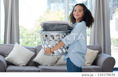 Portrait, laundry and spring cleaning with a woman in the living room of her home carrying a basket. Happy, smile and housework with a young female cleaner carrying fresh washing in her apartment 134170639