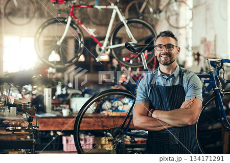 Portrait, smile and repair man in bicycle shop with arms crossed working in store. Face, bike mechanic and confident male person from Canada with happiness, glasses and mature in cycling workshop. 134171291