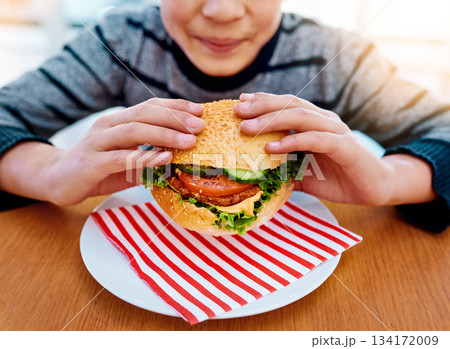 Child, hands and eating burger on table for delicious lunch, meal or food with healthy vegetables at home. Hand of hungry little boy holding beef hamburger for fresh dinner, nutrition or vitamins Child, hands and eating burger on table for delicious lunch, meal or food with healthy vegetables at home. Hand of hungry little boy holding beef hamburger for fresh dinner, nutrition or vitamins 134172009