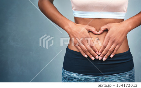 Heart, fitness and hands of a woman on a stomach isolated on a dark background in studio. Wellness, gut health and a girl with shape for love of body, weight loss and abdomen digestion on backdrop 134172012