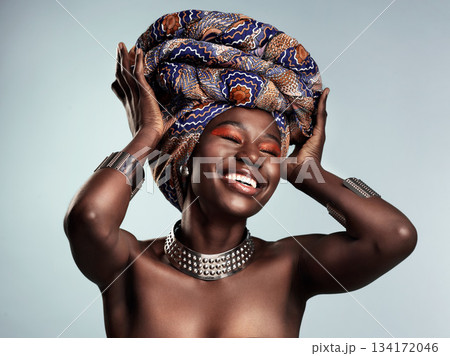 Beauty, black woman and laughing with African turban and smile in a studio. Isolated, grey background traditional makeup with a young female model with culture crown and fashion with cosmetics 134172046