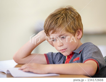 School, education and a boy reading a book at his desk in a classroom for studying or child development. Kids, learning and bored with a young male student child in class to study for an exam or test 134172608