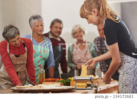 Food, senior cooking class and a woman teaching people in the kitchen of a home for meal preparation. Pasta maker, equipment and learning with mature friends watching a female chef follow a recipe 134172681