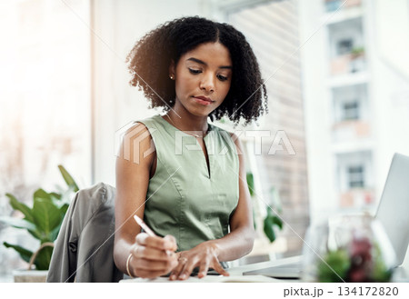 Corporate, black business woman writing in book and at laptop sitting at desk in her office. Planning schedule, reminder and focused African female worker in workplace write notes on information 134172820