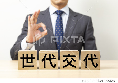 「世代交代」と書かれたブロックとOKポーズをするビジネスマン 134172825