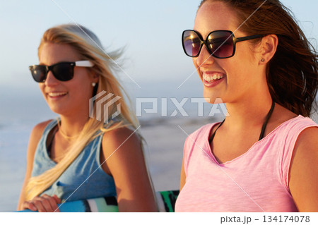 Summer, beach and woman friends surfing outdoor in nature together while on tropical holiday or vacation. Smile, sunglasses and a happy young female surfer with her friend on the coast to surf 134174078