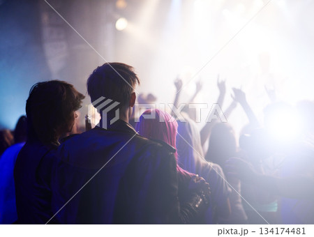 Dance, rock and friends in crowd at music festival from back, watching live band performance on stage. Audience in arena, lights and group of people at party, fans of musician at concert together. 134174481