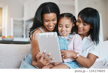 Family, tablet and child on a children education app with mother and grandparent at home. Happiness, bonding and kid game on technology with a young girl smile from mom and grandmother help on couch 134174605