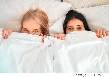 Above, portrait and women covering with blanket for hiding, shy and cold in a bed. Sleep, relax and friends with a duvet to cover face for happiness, funny and warmth in the bedroom together Above, portrait and women covering with blanket for hiding, shy and cold in a bed. Sleep, relax and friends with a duvet to cover face for happiness, funny and warmth in the bedroom together 134175006