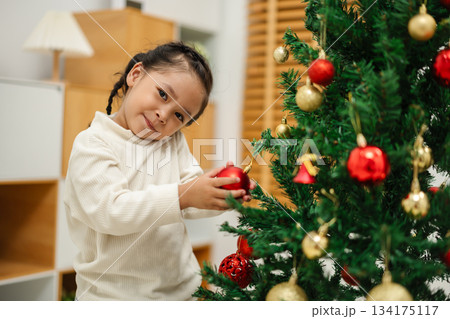 toddler girl decorating toy ball on Christmas tree at home toddler girl decorating toy ball on Christmas tree at home 134175117