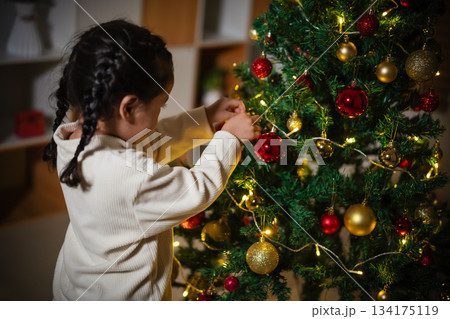 toddler girl decorating Christmas tree in home at night 134175119