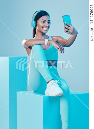 Woman, fitness and selfie in studio with headphones, wellness and training clothes by background. Gen z model, training and fashion with streaming music, body goals or exercise for health by backdrop 134176098