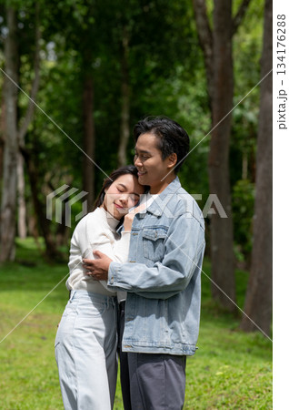 Young asian couple a woman holding and resting head on man's chest while standing outdoors in park. Young asian couple a woman holding and resting head on man's chest while standing outdoors in park. 134176288