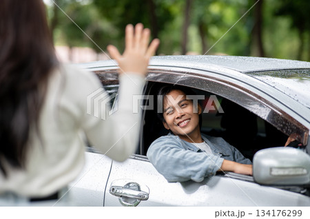 Happy young asian man putting arm out of car window with raindrops on roof as waiting for girlfriend Happy young asian man putting arm out of car window with raindrops on roof as waiting for girlfriend 134176299
