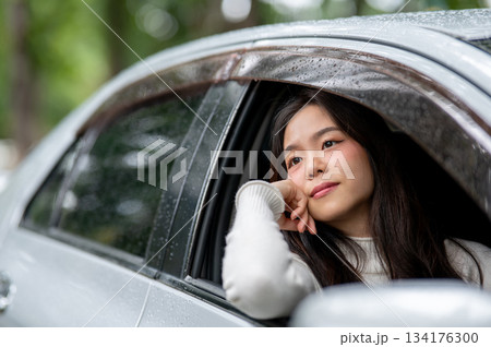 Young asian woman resting head on hand putting an arm out of the car window with raindrops on roof. Young asian woman resting head on hand putting an arm out of the car window with raindrops on roof. 134176300