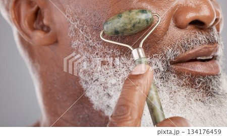 Face roller, closeup and senior man with skincare, stone and dermatology product for skin glow. Elderly, cheek and facial roll of African male model doing self care for grooming with jade for beauty Face roller, closeup and senior man with skincare, stone and dermatology product for skin glow. Elderly, cheek and facial roll of African male model doing self care for grooming with jade for beauty 134176459