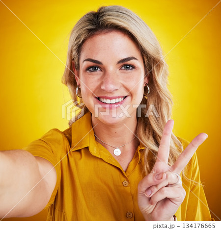 Selfie, portrait and peace with a woman on a yellow background in studio looking happy. Face, smile and hand gesture with an attractive young female model showing v emoji, symbol or social media pov 134176665