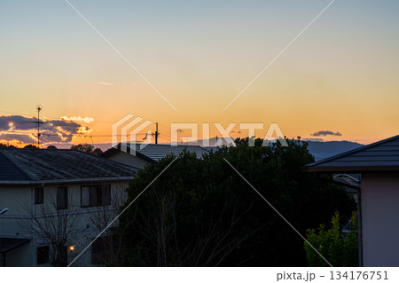 奈良市街地の住宅街で日没後黄金色に縁どられた夕焼け雲と黄金色の空を背景に浮かび上がる生駒山 134176751
