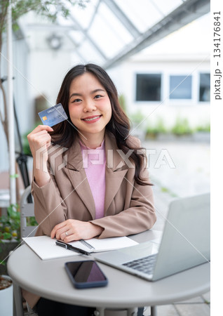 Asian business woman or office worker holding a credit card while sitting with laptop at cafe table 134176841