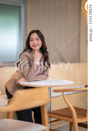 Young asian woman puts a hand under chin while sitting on sofa bench at table in cafe or coffee shop 134176874