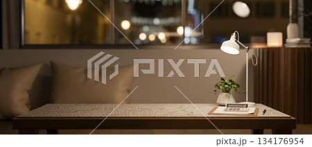 Calculator over clipboard with pot plant and lamp on marble table across sofa and window in dim room Calculator over clipboard with pot plant and lamp on marble table across sofa and window in dim room 134176954